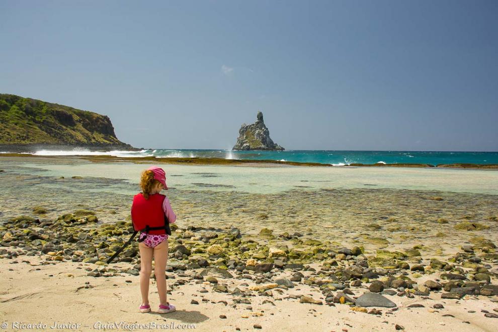 Imagem de uma menina com colete salva vidas aguadando para mergulhar na Praia do Atalaia.